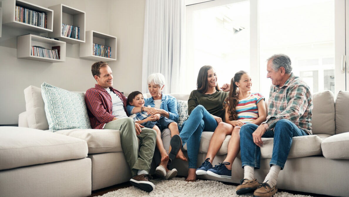 Mehrere Personen unterschiedlichen Alters sitzen nebeneinander auf einem Sofa und lächeln.