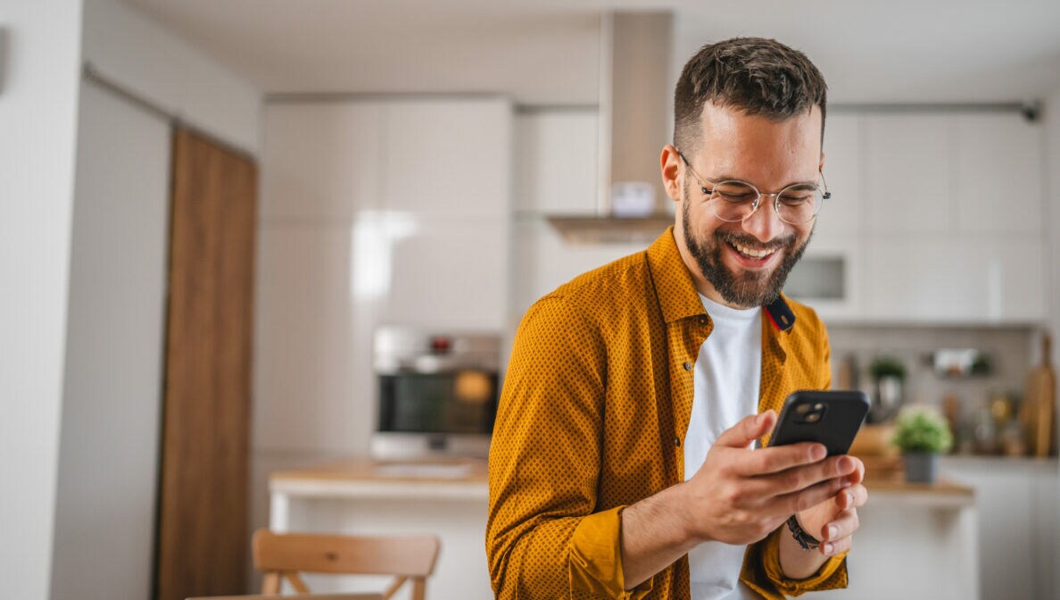 Eine Person hält ein Smartphone in den Händen und blickt lächelnd drauf.