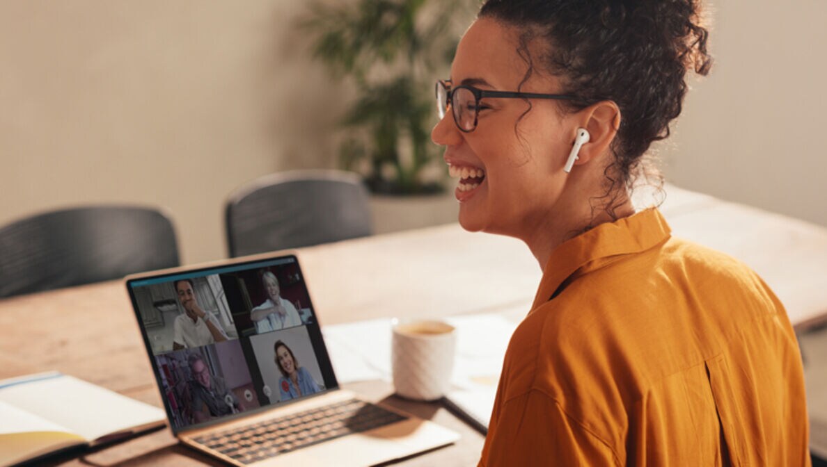 Frau sitzt in einem Online Meeting und lacht.