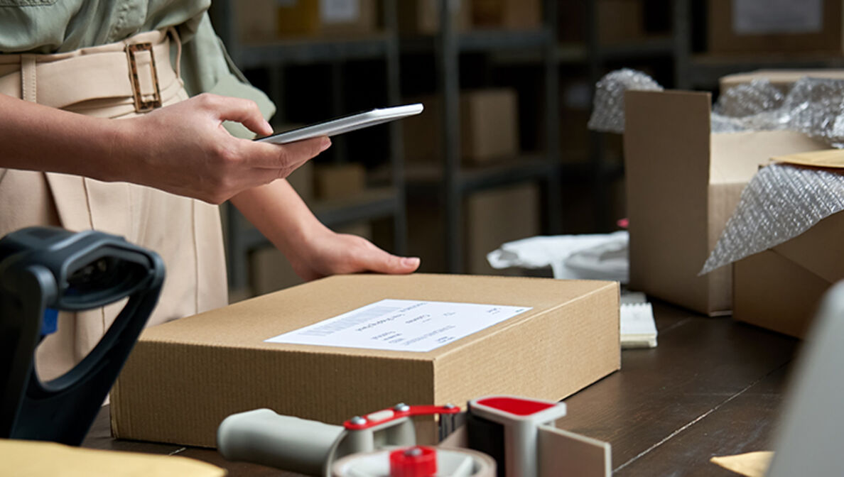 Frau im Paketlager breitet ein Paket für den Versand vor.