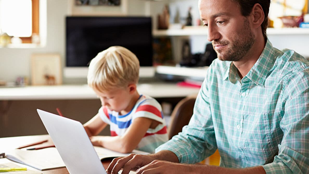 Blogbild: Person arbeitet am laptop während ein Kind daneben Hausaufgaben macht