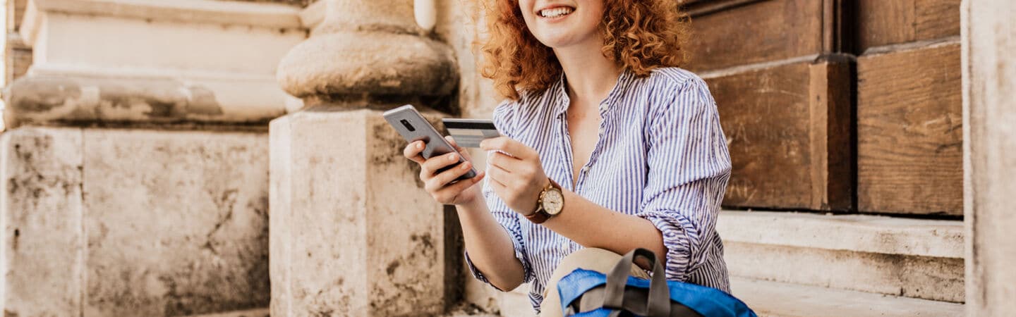 Junge Frau auf einer Treppe sitzend mit Kreditkarte und Smartphone in der Hand