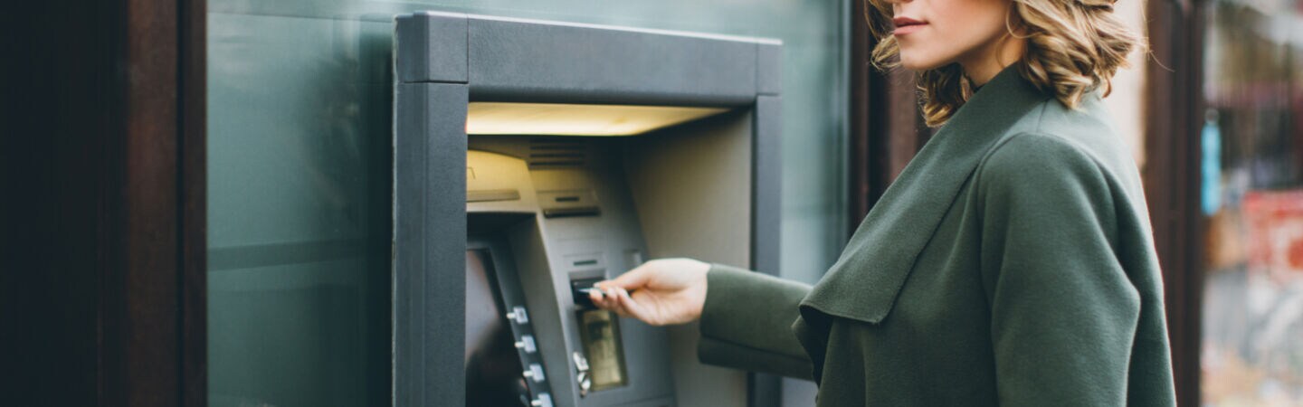 Eine junge Frau schiebt eine Karte in einen Geldautomaten