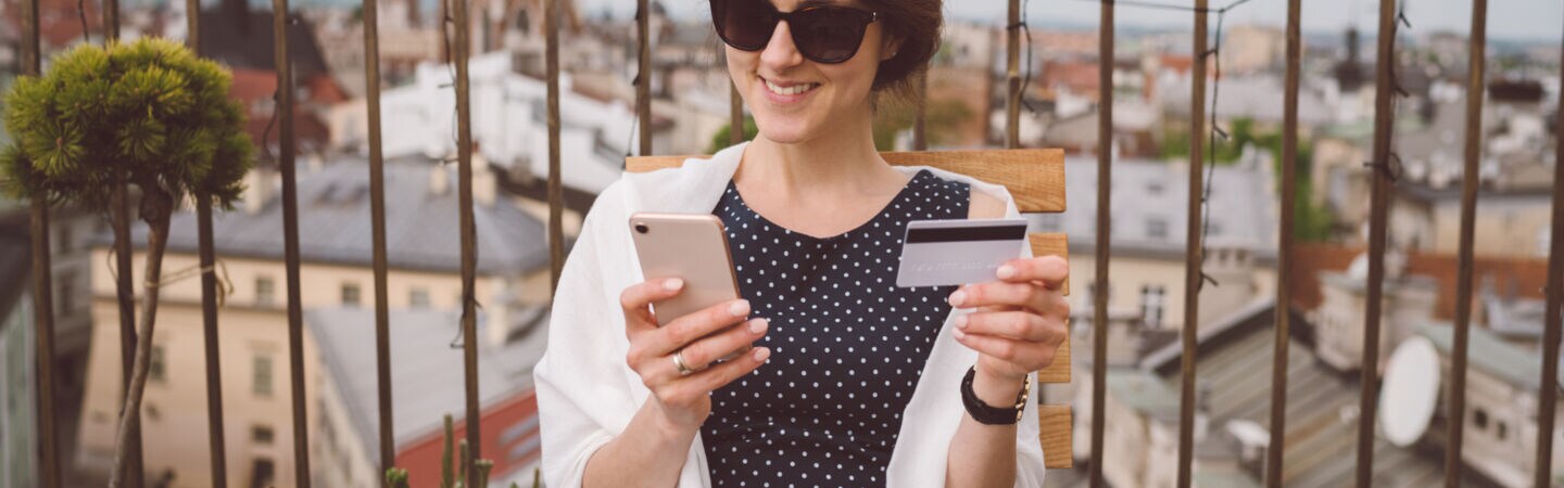 Eine Person sitzt auf einer Terrasse und hält ein Smartphone sowie eine Bankkarte in den Händen.