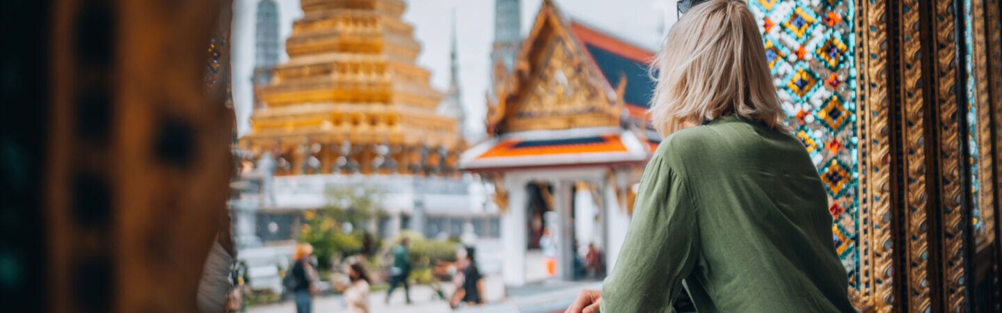 Eine Person blickt aus einem prunkvoll verzierten Fensterrahmen auf goldbesetzte Tempel.