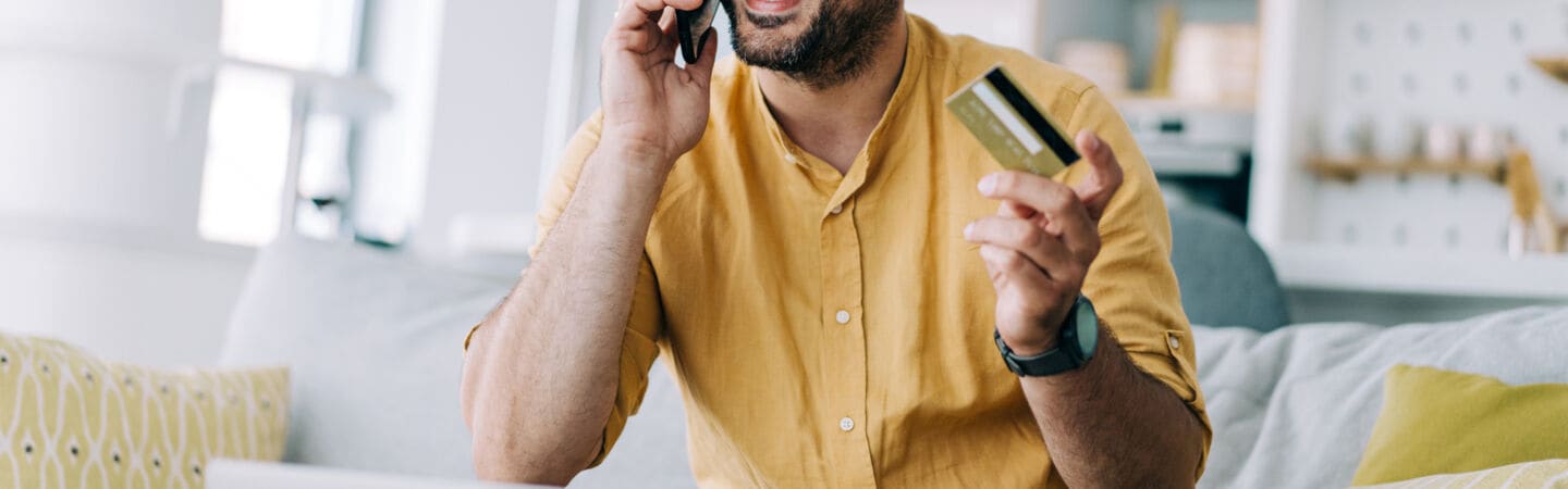 Eine Person sitzt telefonierend auf einem Sofa und hält eine goldene Kreditkarte in der Hand.