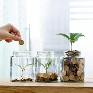 Eine Hand wirft Münzen in Gläser. Aus den Münzen wachsen Pflanzen – je mehr Münzen, desto größer die Pflanze.