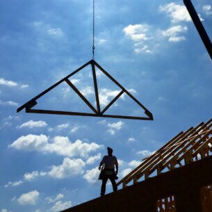 Ein Handwerker auf dem Dach und ein heranbefördertes Giebelteil aus Holz