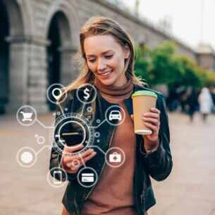 Junge Frau in der Stadt mit Kaffeebecher in der einen und Smartphone in der anderen Hand