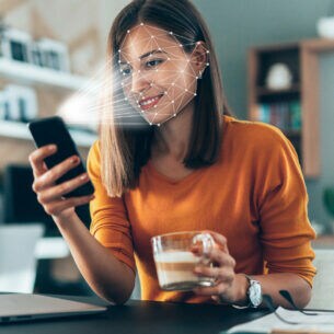 Eine Frau mit Kaffeetasse in der einen Hand und in der anderen ein Smartphone, das Gesichtserkennung durchführt