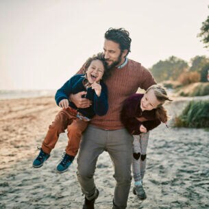 Ein Mann mit zwei lachenden Kindern im Arm am Strand
