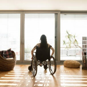 Eine Frau im Rollstuhl, die aus dem Fenster eines Wohnraums blickt