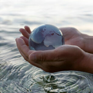 Ein Modell einer Weltkugel, die in zwei Händen gehalten wird, die über Wasser gehalten werden