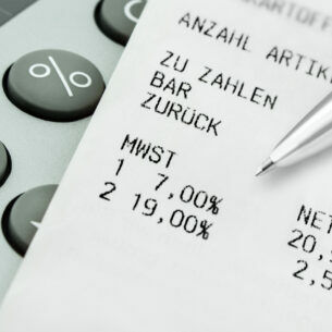 Ein Kassenzettel, der auf einem Taschenrechner liegt und ein Stift, der auf die Mehrwertsteuer auf dem Zettel verweist