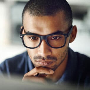 Nahaufnahme des Gesichtes einer Person mit Brille, die konzentriert auf einen Computerbildschirm schaut