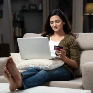 Eine Person sitzt mit Laptop auf dem Sofa und hält eine Kreditkarte in der Hand.