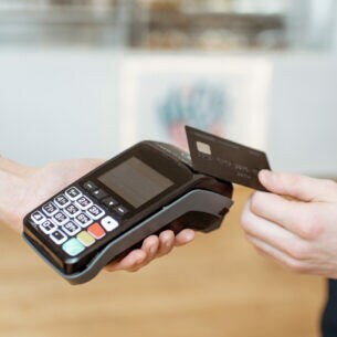 Eine Person hält eine Karte zum Bezahlen an ein Kartenlesegerät, das von einer anderen Person gehalten wird.