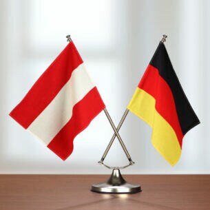 Auf einem Tisch stehen in einer Halterung eine deutsche und österreichische Flagge.