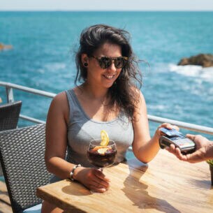 Eine Person sitzt am Meer in einem Restaurant und bezahlt mit einer Bankkarte.