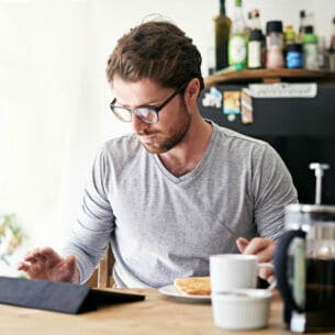 Eine Person sitzt am Frühstückstisch und tippt auf ihr Tablet.