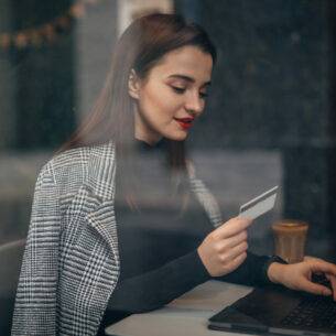 Eine Person sitzt vor einem geöffneten Laptop und hält eine Bankkarte in der Hand.