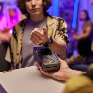 Eine Person hält die Smartwatch an ihrem Arm über ein Zahlungsgerät, das eine ihr hinhält.