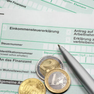 Drei Euromünzen liegen zusammen mit einem Kugelschreiber auf einem Dokument mit dem Titel Einskommenssteuererklärung.