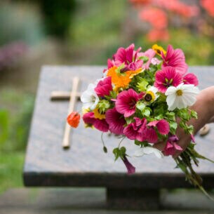 Eine Person legt einen Blumenstrauß vor einem Grabstein mit einem Kreuz nieder.