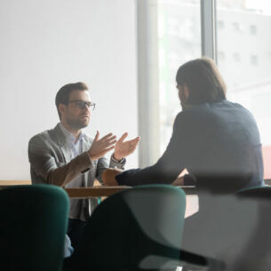 Zwei Personen sitzen sich an einem Konferenztisch gegenüber unter unterhalten sich.