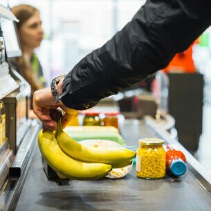 Eine Person steht an einer Supermarktkasse und legt Bananen auf das Förderband.