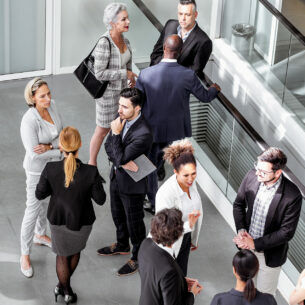 Mehrere Personen in Businesskleidung stehen in kleinen Gruppen in einem hellen Raum.