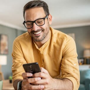 Eine Person lehnt auf einer Kücheninsel und blickt lächelnd auf das Smartphone in ihren Händen.