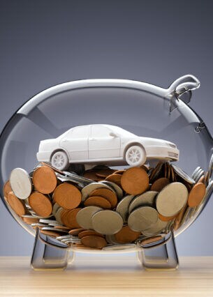 Das Modell eines Autos auf Münzen in einem Sparschwein aus Glas.