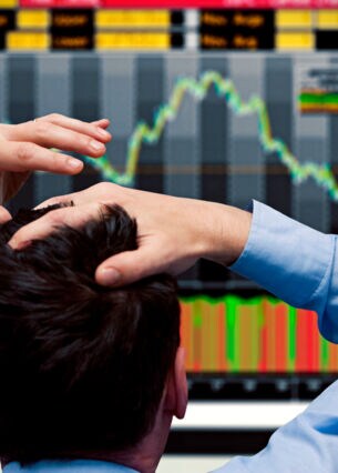 Ein Bildschirm zeigt fallende Börsenkurse und eine Person schlägt die Hände über dem Kopf zusammen.