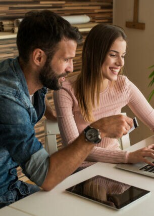Ein junger Mann und eine junge Frau sitzen lächelnd mit einer Kreditkarte vor einem Laptop.