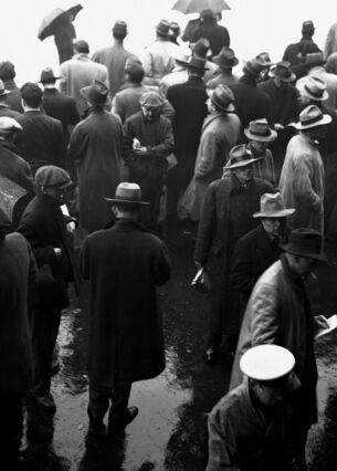 Schwarz-Weiß-Bild von Männern in Mänteln und Hüten, die im Regen auf der Straße stehen