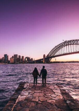 Eine Frau und ein Mann stehen gegenüber der australischen Stadt Sydney und schauen auf die Skyline.