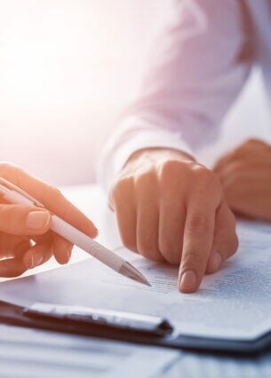 Eine Person zeigt mit einem Stift auf ein Dokument, eine andere Person zeigt mit dem Zeigefinger auf das gleiche Dokument.