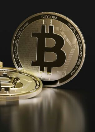 Goldene Bitcoin-Münzen auf einem dunklen, spiegelnden Untergrund.