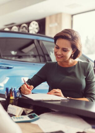 Eine Frau unterschreibt in einem Autohaus einen Vertrag