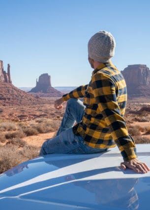 Eine Person sitzt auf der Motorhaube eines Autos und blickt in die Weiten eines US-amerikanischen Nationalparks