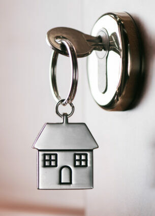 Ein Schlüssel mit Anhänger in Form eines Hauses steckt in einem Türschloss.
