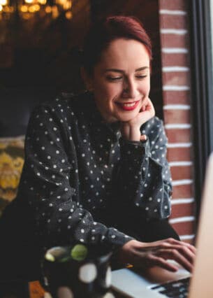 Eine Person sitzt in einem Café und tippt auf ihrem geöffneten Laptop herum.