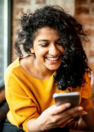 Eine Person sitzt auf einem Ledersofa und blickt lächelnd auf ihr Smartphone.