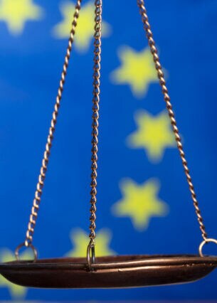 Nahaufnahme einer bronzefarbenen Wage vor einer Europa Flagge