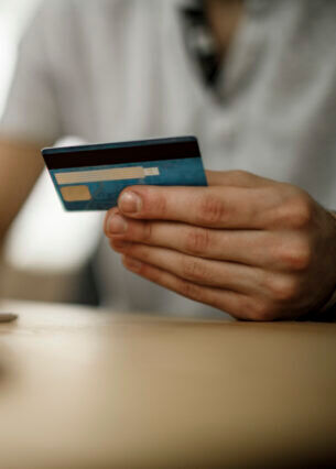 Eine Person tippt mit einer Hand auf einer Tastatur. In der anderen Hand hält sie eine Kreditkarte.