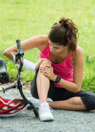 Eine Person hält sich ihr Knie, nachdem sie mit dem Fahrrad gestürzt ist.