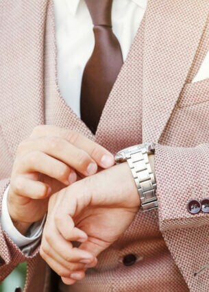 Nahaufnahme einer Person im Anzug, die an der Lünette ihrer Uhr herumspielt.