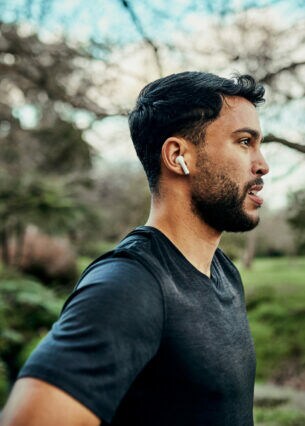 Eine Person joggt durch einen Park und trägt dabei AirPods.