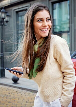 Eine Person steht vor einem roten E-Fahrzeug und hält ein Smartphone in der Hand.